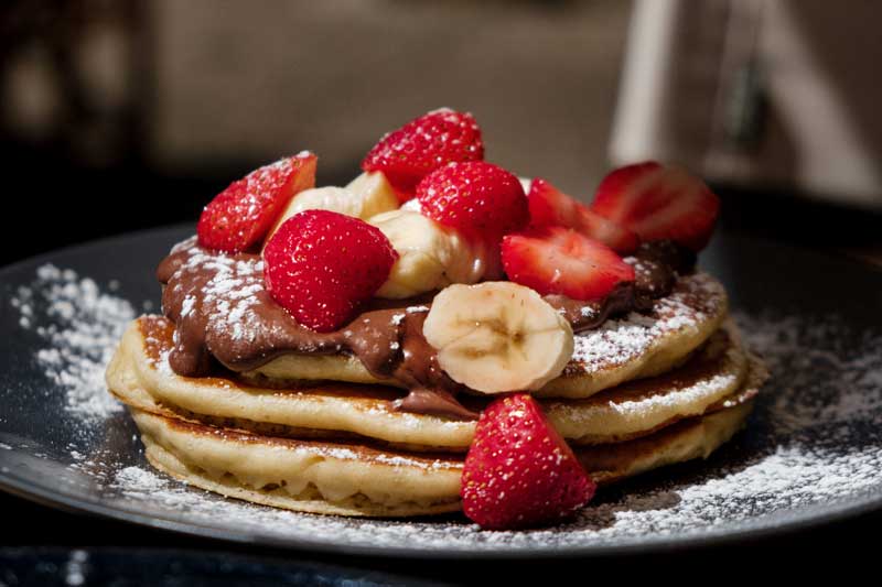 five pancakes sat on a plate with banana and strawberry on top