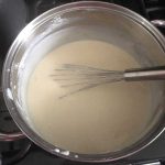 Béchamel Sauce in a silver pan with a silver whisk