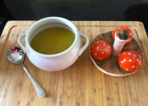 White Soup bowl of Ninja courgette and sweet potato soup in with condiments and a soup spoon on a wooden chopping board