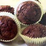 Three chocolate muffins in white paper cases with two muffins in the background