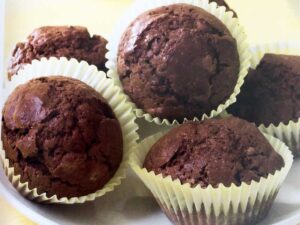Three chocolate muffins in white paper cases with two muffins in the background