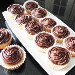 Twelve cupcakes on a granite worktop, ten on a rectangular white plate and two on a black granite worktop