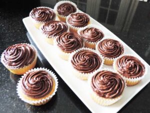 Twelve cupcakes on a granite worktop, ten on a rectangular white plate and two on a black granite worktop