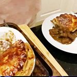 A large steak pie on a wooden chopping board and a white plate with a portion of steak pie on it
