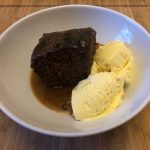 A white bowl with sticky toffee pudding and ice cream