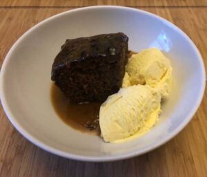 A white bowl with sticky toffee pudding and ice cream
