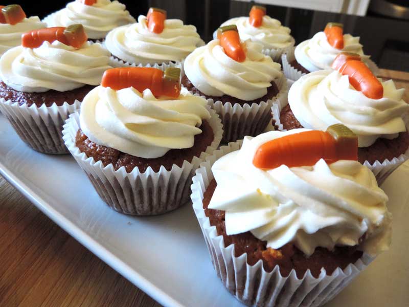Nine cupcakes on a white plate topped with cream cheese frosting and a chocolate carrot